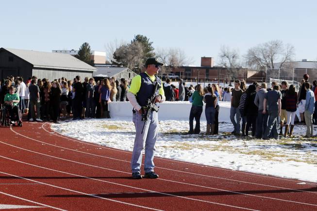 Sheriffs deputies stand guard over students after they were evacuated to the track and football field at Arapahoe High School in Centennial, Colo., on Friday, Dec. 13, 2013, where a student shot at least one other student at a Colorado high school Friday before he apparently killed himself, authorities said. 