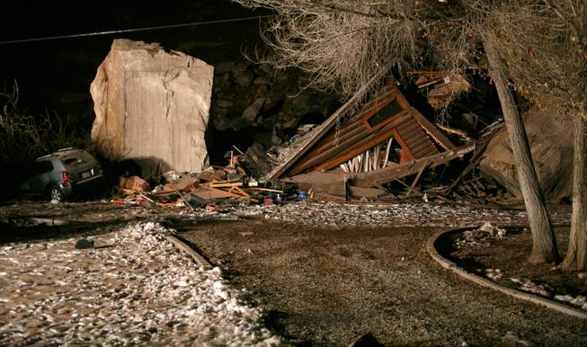 Flood lights from fire engines parked on nearby state Route 9 shine on the rubble of a two-story log home that was crushed by boulders that broke loose from the cliff above it and killed two people inside the home Thursday, Dec. 12, 2013, in Rockville, Utah.