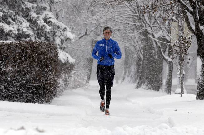 A jogger runs on a snowy sidewalk in Evanston, Ill., on Saturday, Dec. 14, 2013. Snow continued to fall over the Chicago area into northwest Indiana.