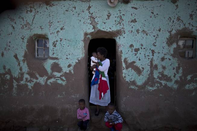 A South African woman, holds her child at the doorway of her home, during the funeral service of former President Nelson Mandela, in Qunu, South Africa, Sunday, Dec. 15, 2013.