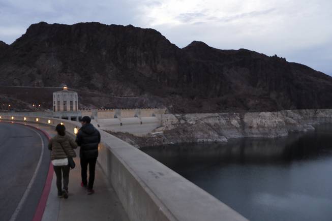 Visitors to Hoover Dam and Lake Mead walk near canyon walls ringed with white mineral deposits where water once lapped indicating the drop in water levels, near Boulder City, Nev., Dec. 18, 2013.