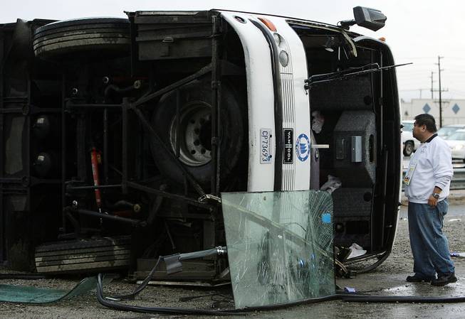 The driver of a tour bus stands next to the bus after it flipped on its side and crashed on wet southbound Interstate 15, half a mile north of the Ontario Avenue onramp, on Thursday, Dec. 19, 2013, in Corona, Calif. 