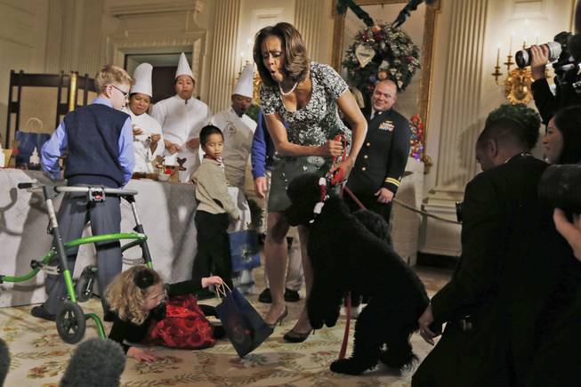 First lady Michelle Obama reacts as Ashtyn Gardner, 2, from Mobile, Ala., loses her balance when she was greeting Sunny, one of the presidential dogs, as children of military families participate in a holiday arts and crafts event in the State Dining Room at the White House in Washington, Wednesday, Dec. 4, 2013. 
