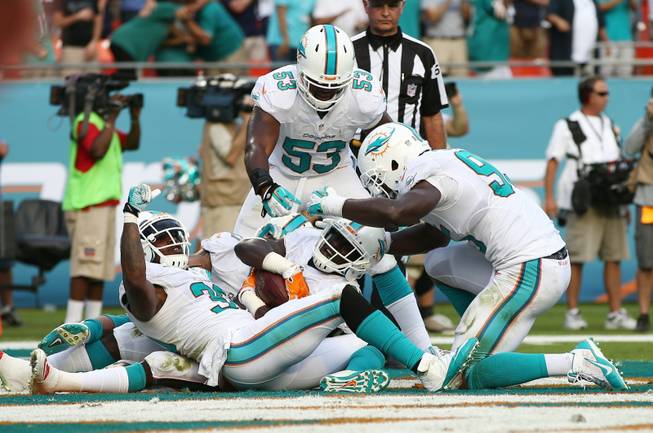 Miami Dolphins Michael Thomas, center, is congratulated by teammates Chris Clemons (30), left, and Jelani Jenkins (53) after Thomas intercepted a pass intended for New England Patriots wide receiver Austin Collie (10) during the second half of an NFL football game, Sunday, Dec. 15, 2013, in Miami Gardens, Fla. The Dolphins defeated the Patriots 24-20.
