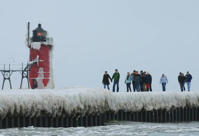 People walk along an ice-covered pier near the South Haven Lighthouse on Saturday, Dec. 21, 2013, in South Haven, Mich. 