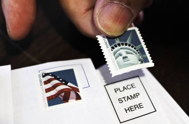 In this Dec. 5, 2011, photo, a customer places first-class stamps on envelopes at a U.S. Post Office in San Jose, Calif.