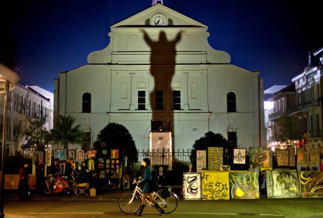 In this Friday, Feb. 1, 2013, file photo, a pedestrian walks her bicycle past a silhouette of Jesus Christ projected against the Cathedral-Basilica of Saint Louis King of France in New Orleans, two days ahead of the NFL Super Bowl football game between the San Francisco 49ers and the Baltimore Ravens. "I find it fascinating that that's what people really want to know: What race was Jesus? That's says a lot about us, about Americans today," said Edward Blum, co-author of "The Color of Christ: The Son of God and the Saga of Race in America."