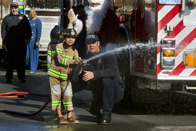 Isaac Cambero, 8, sprays a fire hose on Christmas morning as firefighters from Operation FireH.E.A.T. (Holiday Emergency Assistance Team) came to visit and deliver presents Wednesday, Dec. 25, 2013.