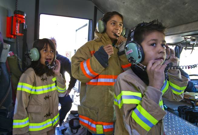 Lupita Cambero, 10, with siblings Ashley, 11, and Isaac, 8, try on firefighter equipment during a visit on Christmas morning from Operation FireH.E.A.T. (Holiday Emergency Assistance Team) on Wednesday, Dec. 25, 2013.