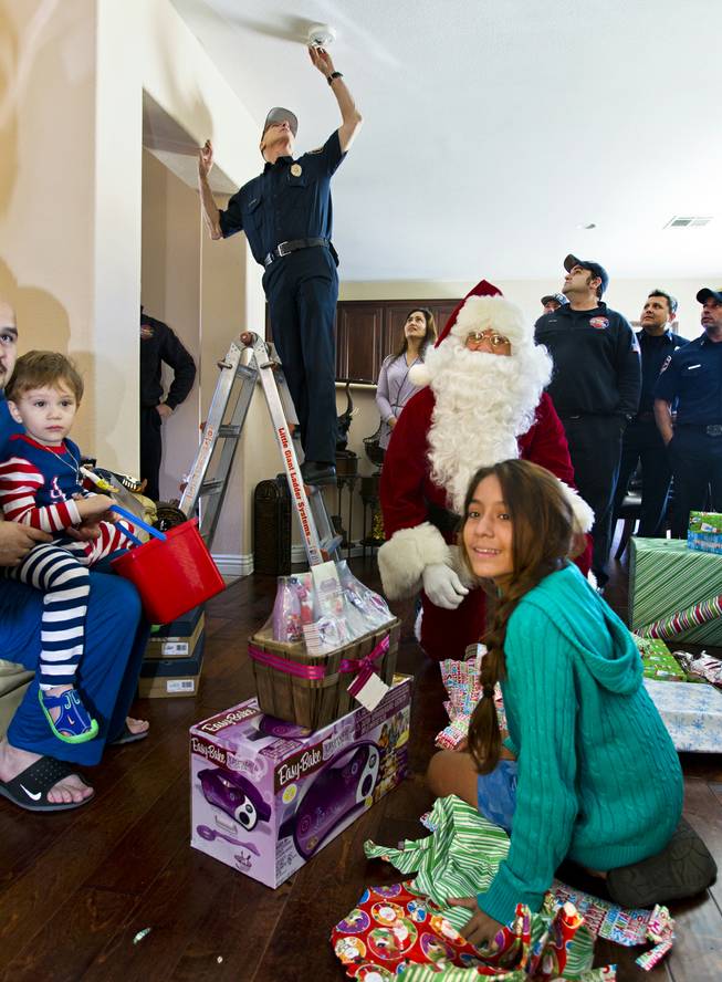 Ashley Cambero, 11, looks from a present with Santa and a group from Operation FireH.E.A.T. (Holiday Emergency Assistance Team) on Wednesday, Dec. 25, 2013, who delivered gifts to her family.