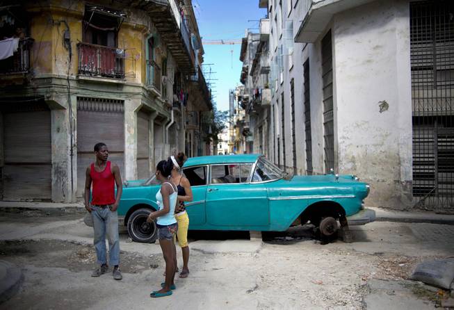 People talk as they stand in a street blocked by a broken down classic car in Havana, Cuba, Thursday, Dec. 26, 2013. 