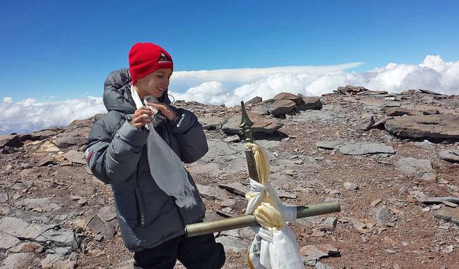 This Tuesday, Dec. 24, 2013, photo released by Lhawang Dhondup shows Tyler Armstrong of Southern California standing by a cross on the summit of Aconcagua Mountain in Argentina. 