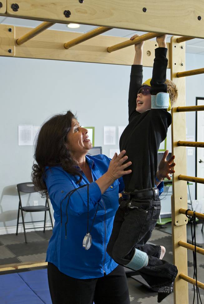 Dr. Susan DeVito steadies Chase Black, 7, as he hangs on the monkey bars for strength conditioning within the Brain Balance Achievement Center on Monday, Dec. 30, 2013.