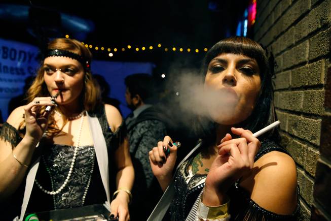 Partygoers smoke marijuana, left, and cigarettes during a Prohibition-era themed New Year's Eve party celebrating the start of retail pot sales, at a bar in Denver, late Tuesday Dec. 31, 2013. Colorado is to begin marijuana retail sales on Jan. 1, a day some are calling "Green Wednesday."