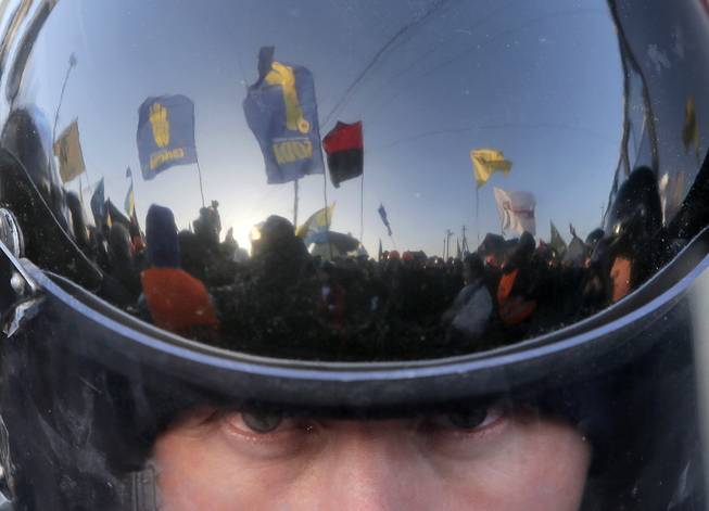 A thousand-strong pro-European Union rally is reflected in the surface of a riot police officer's helmet as he guards the way to Ukrainian President Viktor Yanukovychs country residence of Mezhygirya outside Kiev, Ukraine, Sunday, Dec. 29, 2013. Hundreds of riot police blocked approaches to Mezhygirya as protesters demanded Yanukovych's resignation over his decision to ditch a pact with the European Union in favor of closer ties with Russia. 