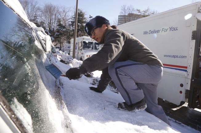 US Postal Service letter carrier Danny Kim clears snow and ice as he climbs on the hood of his mail delivery truck in the parking lot at the U.S. Post Office in Bethesda, Md., Friday, Jan. 3, 2014. Kim said that despite the storm resulting in many closing of local school systems, he and his colleagues were working on an unchanged schedule. A winter storm that swept across the Midwest this week blew through the Northeast and its biggest cities on Friday, producing more than a foot of snow in spots, giving rise to wind gusts that threatened trees and power lines, and leaving bone-chilling cold in its wake. (AP Photo/Charles Dharapak)