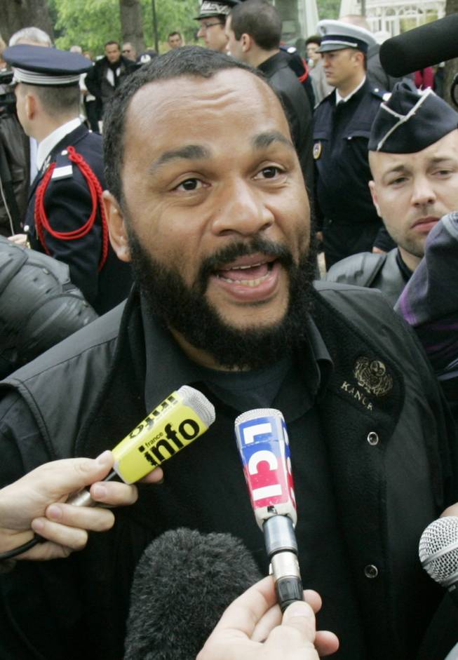 In this May 13, 2009, file photo, controversial French comic Dieudonne M'Bala M'Bala, known as Dieudonne, answers reporters as he heads for the interior Ministry to submit a list of candidates for the upcoming European elections, in Paris. The Paris prosecutor's office said Thursday Jan. 2, 2013, it is investigating threats against a comedian the French interior minister wants banned from the stage for what he says are racist and anti-Semitic performances.