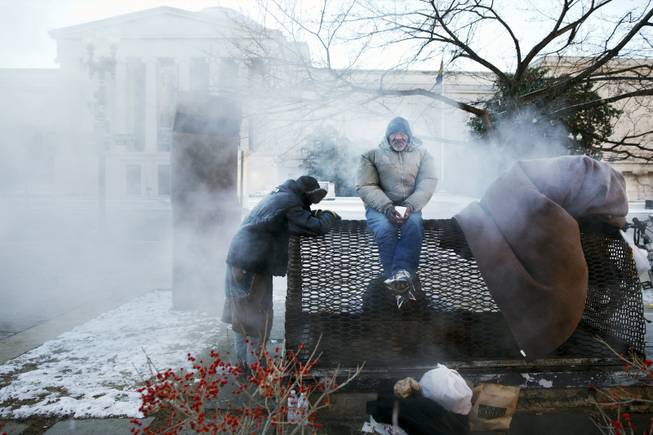 Four homeless men warm themselves on a steam grate by the Federal Trade Commission, blocks from the Capitol, during frigid temperatures in Washington on Saturday, Jan. 4, 2014. 