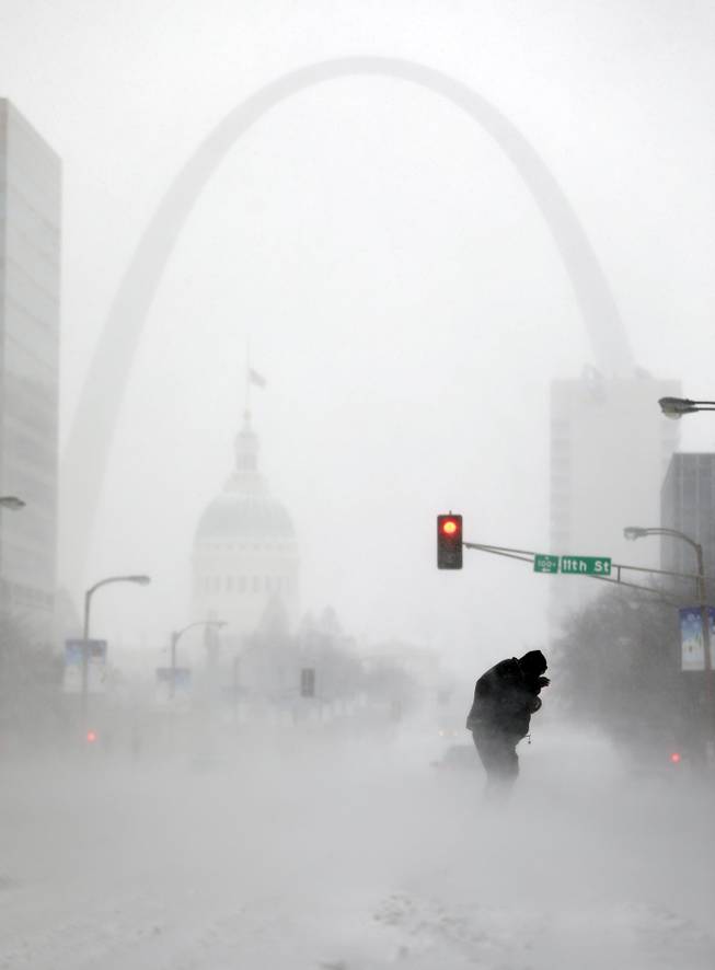 A person struggles to cross a street in blowing and falling snow as the Gateway Arch appears in the distance Sunday, Jan. 5, 2014, in St. Louis. Snow that began in parts of Missouri Saturday night picked up intensity after dawn Sunday with several inches of snow on the ground by midmorning and more on the way.