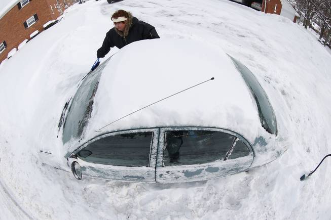 In an imagge made with a fisheye lens, Marguerite Johnston uncovers her car in Grosse Pointe, Mich., Monday, Jan. 6, 2014. Michigan residents are preparing for diving temperatures as they dig out from more than 15 inches of snow in places.
