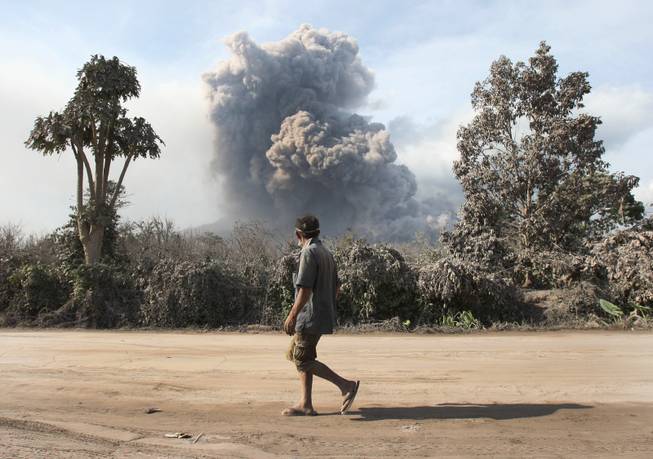 A man watches as Mount Sinabung spews volcanic materials in Sibintun, North Sumatra, Indonesia, Wednesday, Jan. 8, 2014. The volcano has sporadically erupted since September, forcing thousands of people who live around it slopes to flee their homes. 