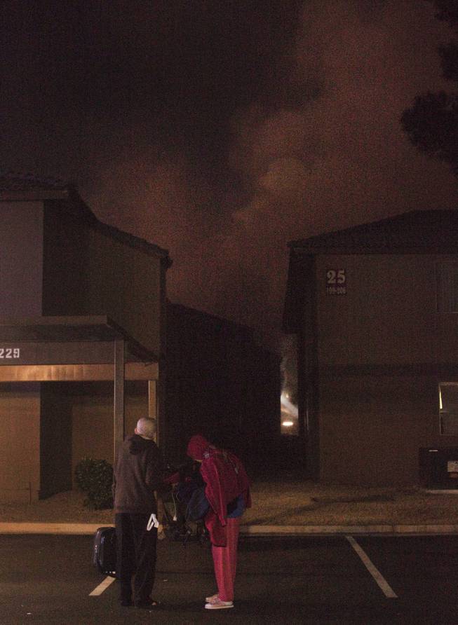 Century Village apartments residents Freddie Veloro and his wife, Tessie, carry some of their belongings as smoke from a fire billows in the background. Clark County firefighters responded to a blaze at the apartment complex early Thursday, Jan. 9, 2014. 
