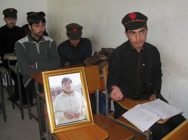 Pakistani students sit next to a picture of 17-year-old classmate Aitzaz Hasan, who residents and police say died this week while trying to stop a suicide bomber who was targeting his school in a remote village in Hangu, Pakistan, Friday, Jan. 10, 2014.