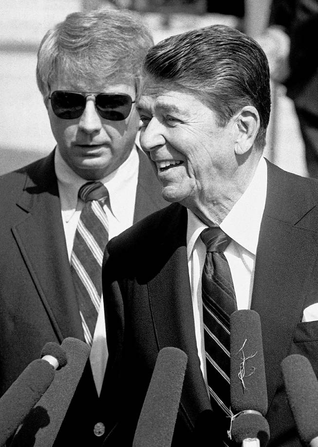 In this Sept. 2, 1984, file photo, U.S. President Reagan, flanked by Deputy Press Secretary Larry Speakes, talks to reporters on the South Lawn of the White House, in Washington, as he prepared to leave for California. 