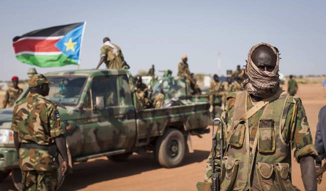 A South Sudanese government soldier stands with others near their vehicles, after government forces on Friday retook from rebel forces the provincial capital of Bentiu, in Unity State, South Sudan, Sunday, Jan 12, 2014.