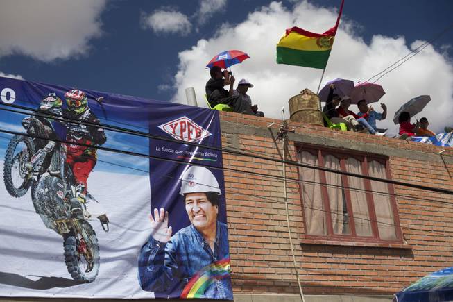A poster with a photo of Bolivian President Evo Morales to promote Bolivia's state oil company decorates a building where people wait to see the motorcycles arriving at the end of the seventh stage of the Dakar Rally in Uyuni, Bolivia, Sunday, Jan. 12, 2014. 