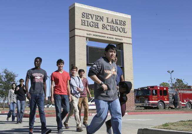 Students pass by Seven Lakes High School after being evacuated and released from school for the day Monday, Jan. 13, 2014, in Katy, Texas. A bomb squad was called to the school after a backpack with a potentially explosive devise was found. The Katy school district says a student is in custody.