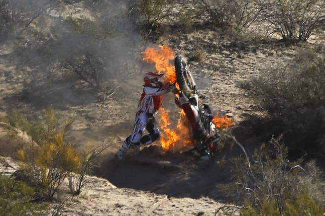 Honda rider Paulo Goncalves of Portugal lifts his motorcycle to try to put off the fire during the fifth stage of the Dakar Rally between the cities of Chilecito and Tucuman in San MIguel de Tucuman, Argentina, Thursday, Jan. 9, 2014. 