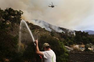 Mark Davis gives a thumb up toward a helicopter as he sprays water around his property on Thursday, Jan. 16, 2014, in Azusa, Calif. 