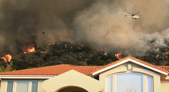 A firefighting helicopter passes over the hills behind homes as a wildfire burns just north of the San Gabriel Valley community of Glendora, Calif., on Thursday, Jan 16, 2014. 
