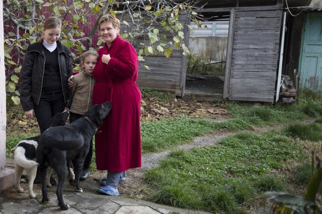 In this photo taken on Wednesday, Nov. 27, 2013, Alexandra Krivchenko, right, and her children, center, play with the dogs in the yard of a house sandwiched between the railway and a federal highway (seen in the background) in the village of Vesyoloye outside Sochi, Russia.