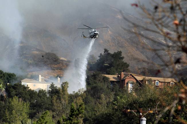 A firefighting helicopter makes a water drop over homes in Glendora, Calif. as a wildfire burns in the hills just north of the San Gabriel Valley community on Thursday, Jan 16, 2014. 