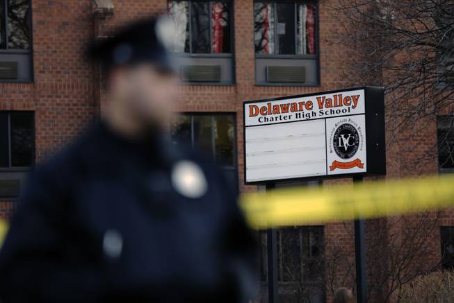 A police stands by caution tape at the Delaware Valley Charter School Friday, Jan. 17, 2014, in Philadelphia. Police say two students have been shot at the Philadelphia high school.