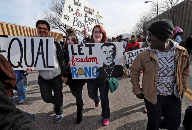 The message on the handmade signs of, from left, William Smith, Victoria Dowdy, and Stephanie Wormald, draw attention from a fellow marcher during the March of Celebration honoring the Rev. Martin Luther King Jr. on Monday, Jan. 20, 2014, in St. Louis. 