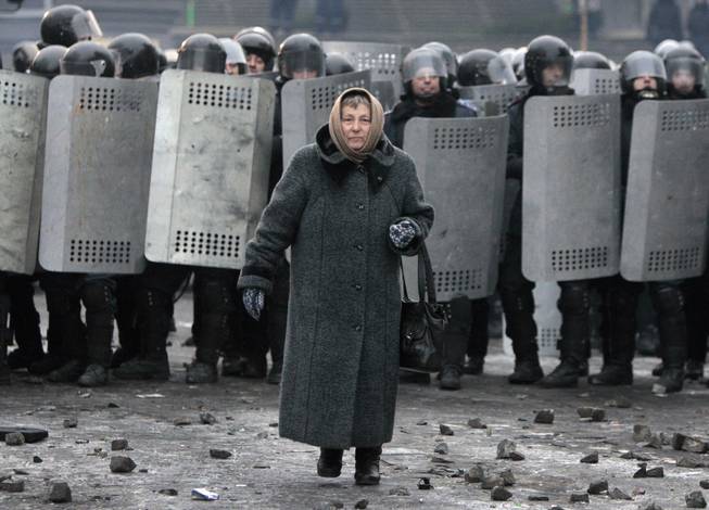 An elderly woman walks from police officers as they block a street during unrest in central Kiev, Ukraine,Tuesday, Jan. 21, 2014. Anti-government protesters have held their ground through a night of violent street clashes in the Ukrainian capital, despite police moving in to dismantle barricades erected in a street leading to government offices. Police attempted to move in on the protest camp early Tuesday, but faced fierce resistance from demonstrators who tossed fire bombs and stones in their direction. 