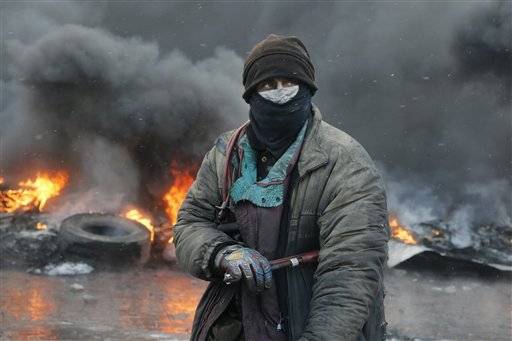 A protester stands at a burning barricades between police and protesters in central Kiev, Ukraine, Thursday Jan. 23, 2014. Thick black smoke from burning tires engulfed parts of downtown Kiev as an ultimatum issued by the opposition to the president to call early election or face street rage was set to expire with no sign of a compromise on Thursday.