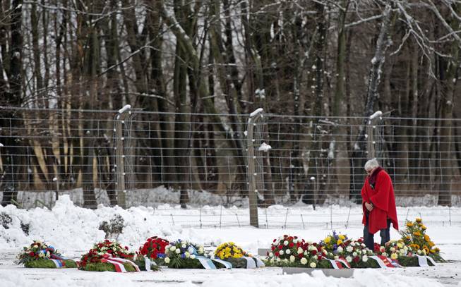 A woman stands between flowers and wreaths during the international Holocaust remembrance day in front of the barbed wire of the former the Nazi concentration camp Buchenwald near Weimar, Germany, Monday, Jan. 27, 2014. 