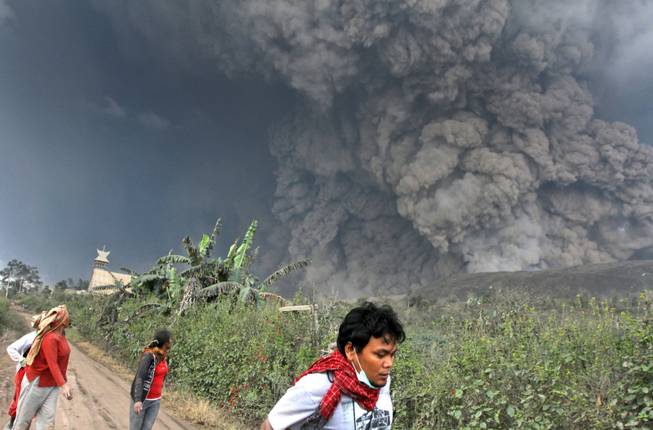 Villagers and a journalist prepare to flee as Mount Sinabung releases pyroclastic flows during an eruption in Namantaran, North Sumatra, Indonesia, on Saturday, Feb. 1, 2014. The rumbling volcano in western Indonesia has unleashed fresh clouds of searing gas, killing several people.