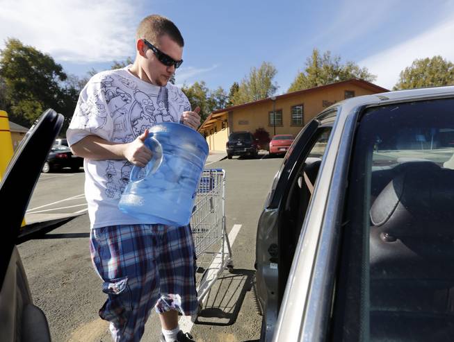 In this photo taken Tuesday, Feb. 4, 2014, Forrest Clark, 25, loads five gallon bottles of water, purchased at a local store, into his car in Willits, Calif.  With local reservoirs holding less than a 100-day supply of water, city leaders have banned lawn watering, car washing and mandated all residents to cut water use. Clark, who said he doesn't like the taste of the local water, buys 10-15 gallons of bottled water a week to help boost the family water supply.