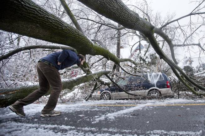 A man inspects an ice covered downed tree that took out an utility line and landed atop a minivan, after a winter storm Wednesday, Feb. 5, 2014, in Philadelphia. Icy conditions have knocked out power to more than 200,000 electric customers in southeastern Pennsylvania and prompted school and legislative delays as well as speed reductions on major roadways. 