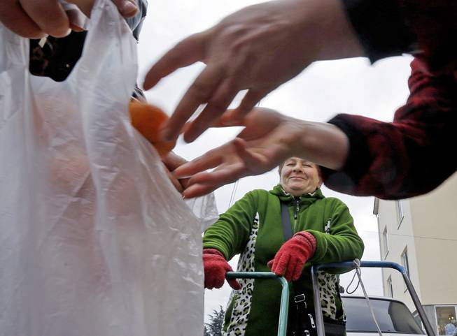Mukhmunad Ashabokova watches as someone puts tangerines in a bag at the Abkhazian border Wednesday, Feb. 5, 2014, near Sochi, Russia. Most days in the tangerine season, she rolls her squat cart loaded down with the fruit across the bridge over Psou River from her garden about two miles inside Abkhazia. 