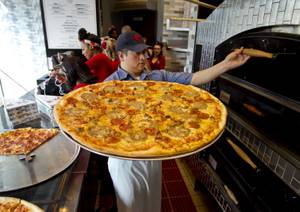 Chef Jorge Torres pulls another freshly baked pie from the oven at Pin-Up Pizza.