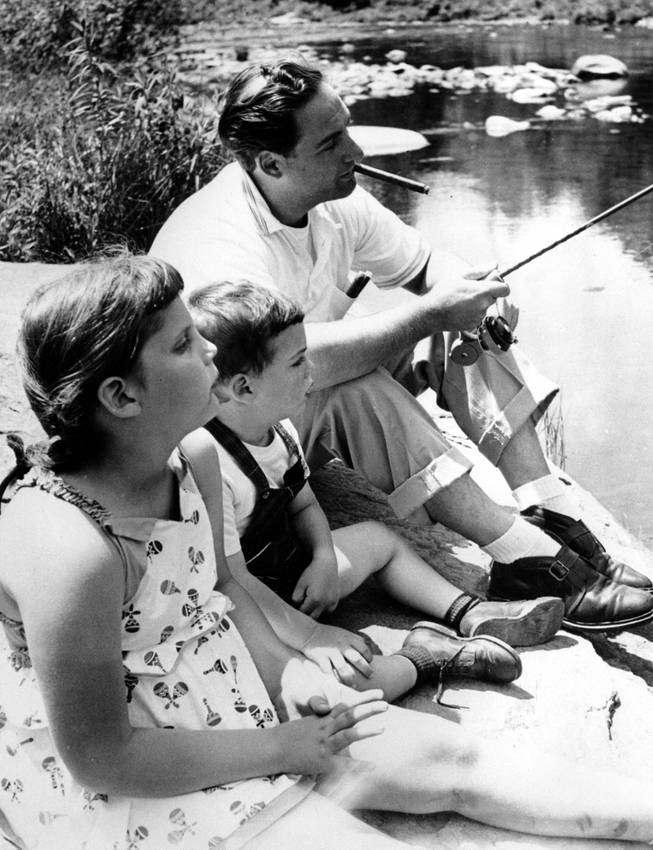 Comedian Sid Caesar relaxes with fishing rod while his children, Shelly, 6, and Ricky, 27 months, sit beside him during their vacation in Upstate New York in June 1954.  