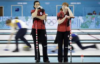 Canada's Jill Officer, left, and Dawn McEwen, right, wait on the sidelines of the ice sheet during the women's curling competition against Britain at the 2014 Winter Olympics, Wednesday, Feb. 12, 2014, in Sochi, Russia.