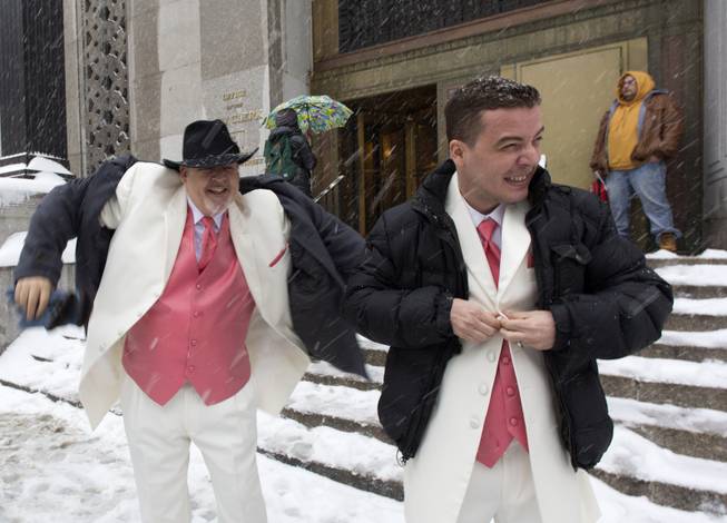 Newlyweds Steve Cosh, left, and Thiago Cardoso pull on their winter jackets as they step out from New York's municipal marriage bureau, Thursday, Feb. 13, 2014. Snow and sleet are falling on the East Coast from North Carolina to New England a day after sleet, snow and ice bombarded the Southeast. 