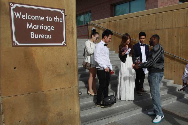 Deshaun Houston talks to Ivy Dinh and Tai Nguyen about the services his wedding chapel provides outside the Marriage Bureau at the Regional Justice Center Friday, Feb. 14, 2014.
